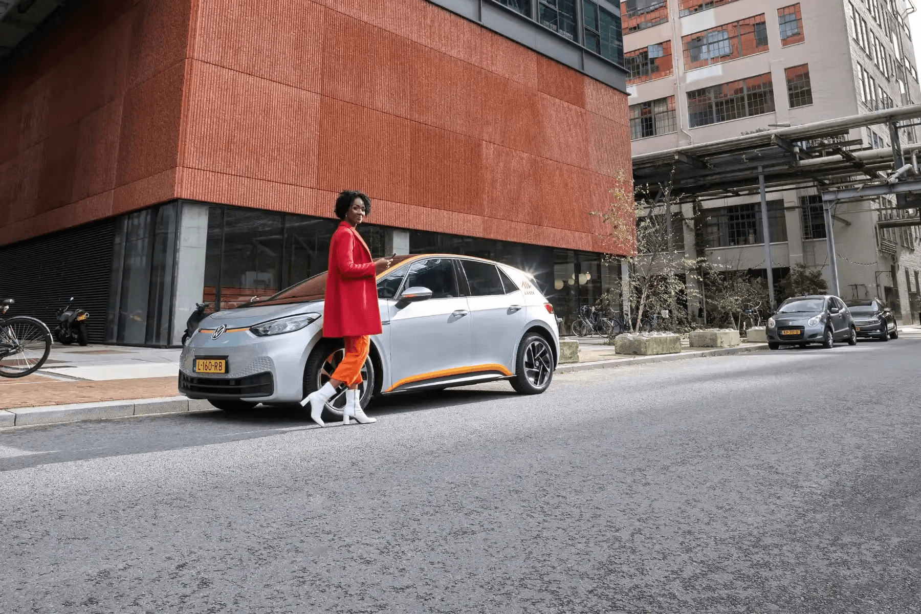 Woman in red coat walking dog past parked car on city street