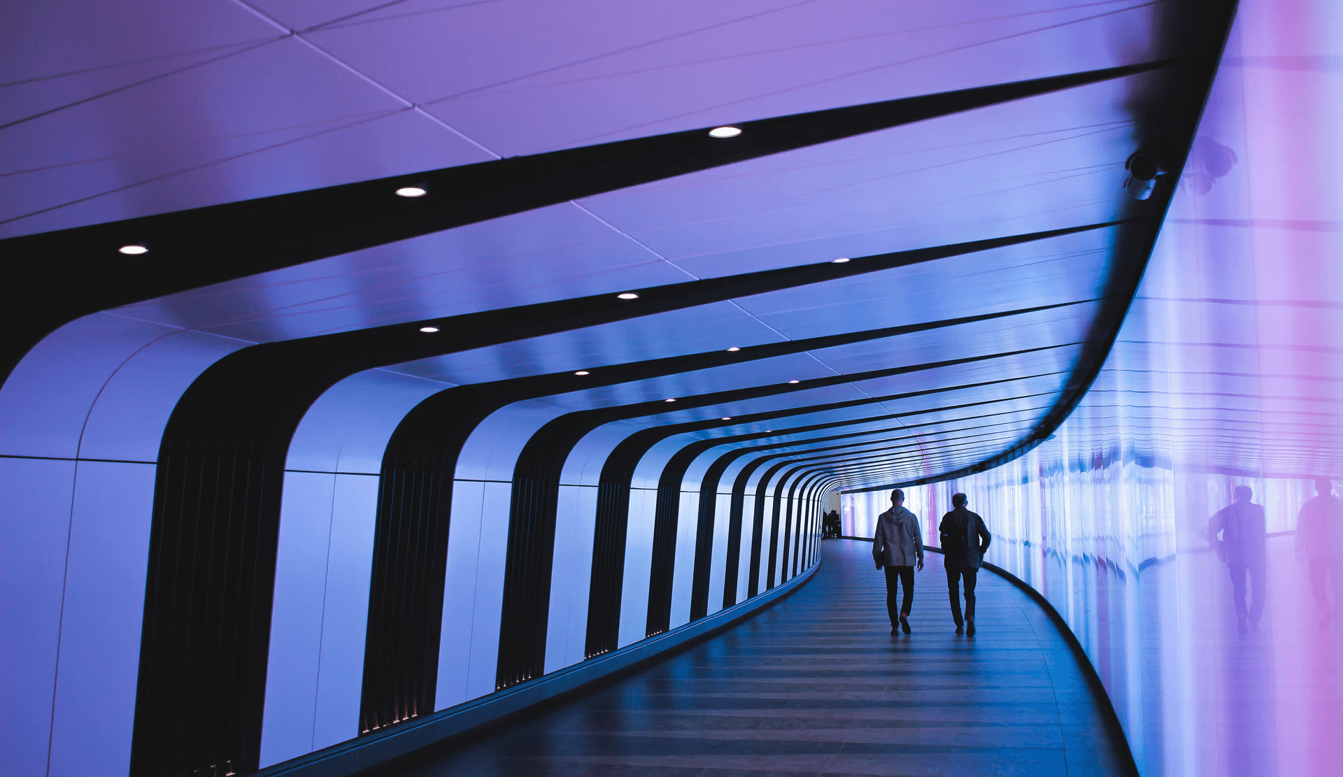Two people walking through a futuristic purple-lit pedestrian tunnel