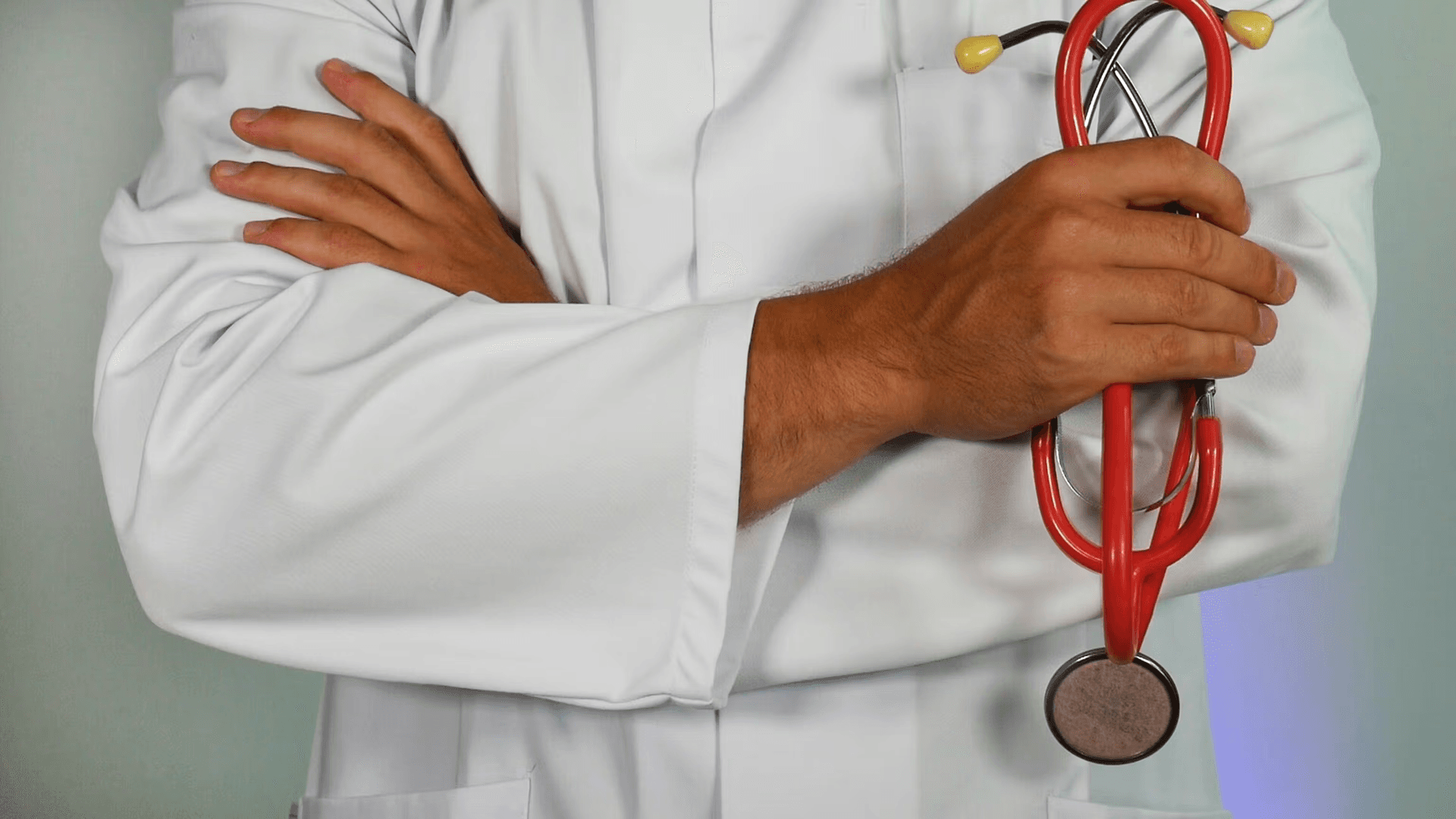Doctor in white coat holding a red stethoscope with arms crossed